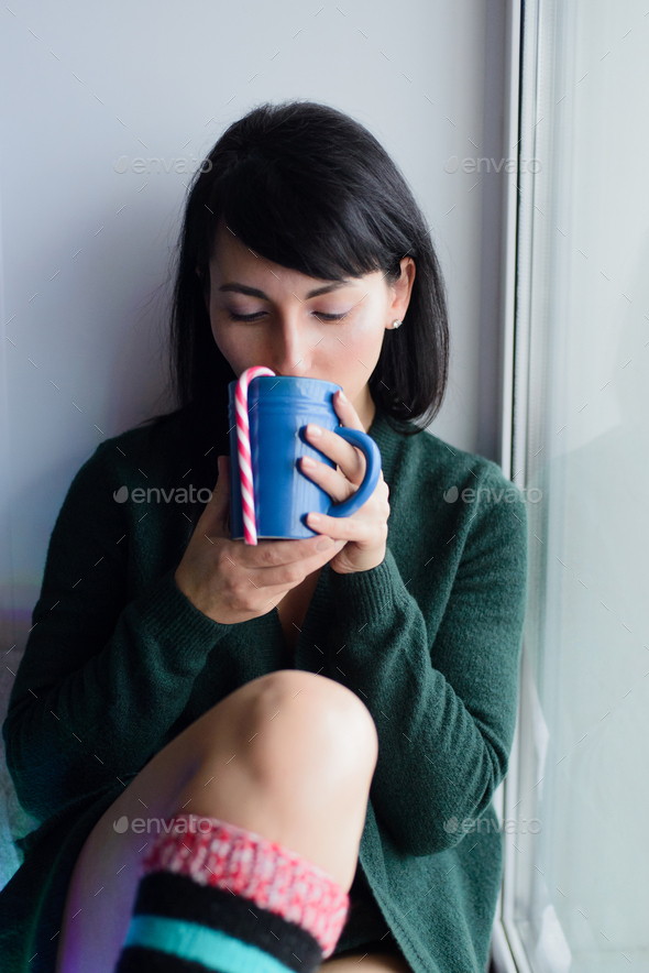 woman on windowsill with beverage and striped candy cane - Stock Photo - Images