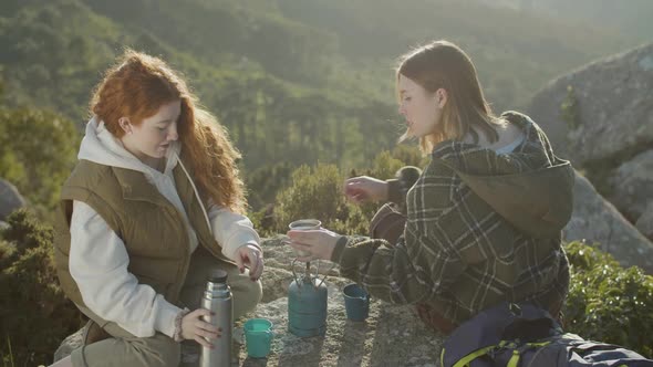 Two Female Tourists Drinking Hot Tea From Thermos alt
