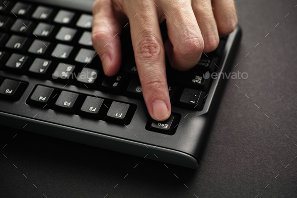 Man\'s finger pressing Escape key on black computer keyboard