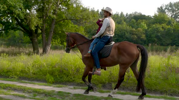Cowboy and His Daughter on Horseback on a Forest Lawn alt