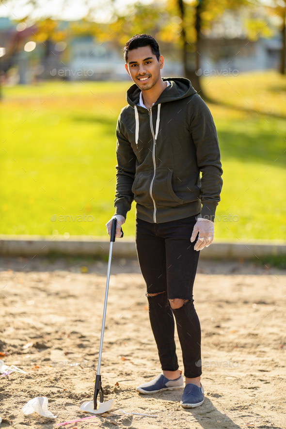 Confident volunteer cleaning park on sunny day - Stock Photo - Images