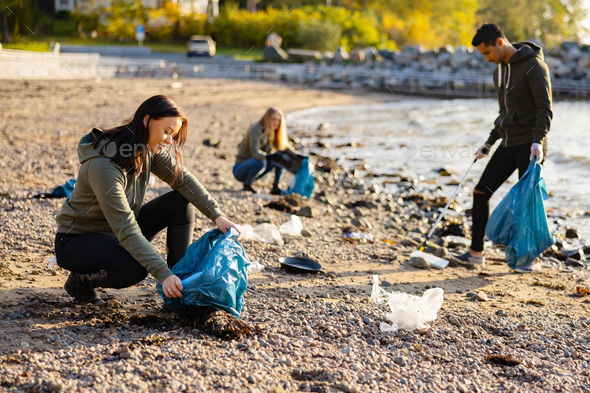 Young woman picking up garbage in bag at beach Stock Photo by kjekol