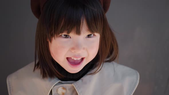 Korean Girl in a Gray Coat and Cap Stands the Street in Spring at the Glass Doors of the Store alt