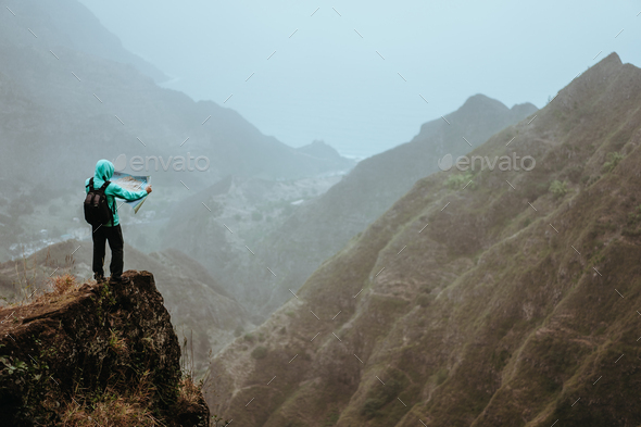 Hiker with map in steep rocky terrain in front of a incredible panorama view of high mountain ranges - Stock Photo - Images