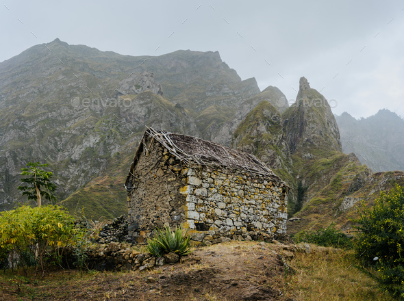 Ruined local storehouse nestled into incredible scenery with steep mountain rocks and vertical peaks - Stock Photo - Images