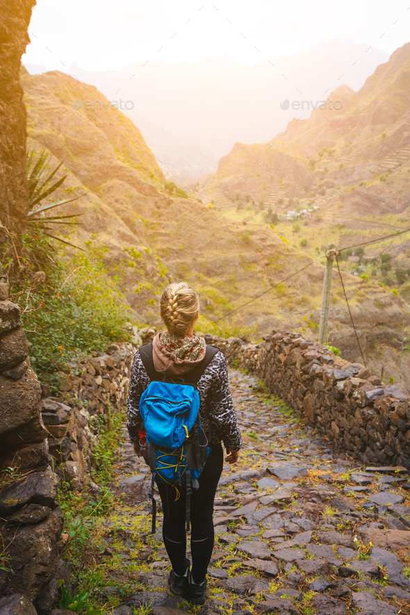 Female hiker with blue backpack staying on the stony cobbled trekking trail leading down to the
