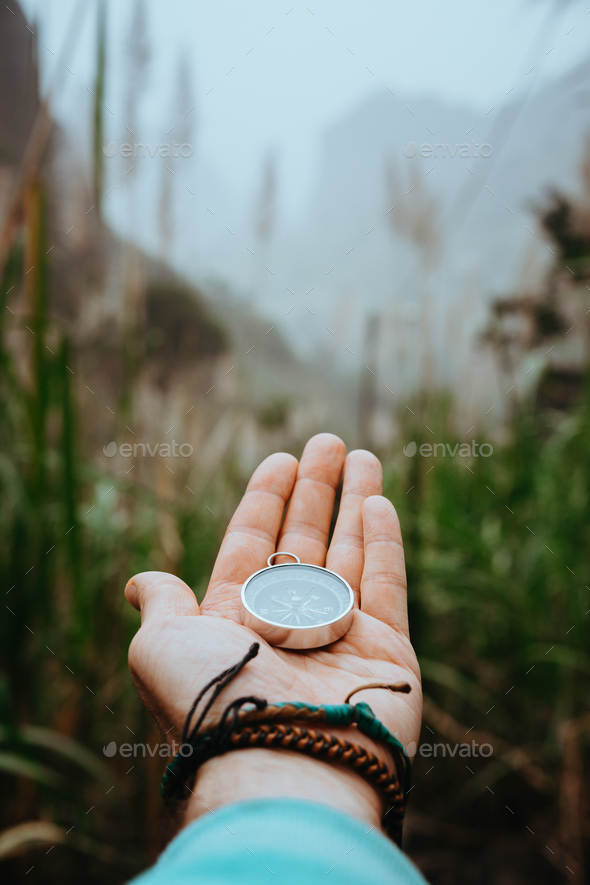 Man arm with compass on the palm stretched out to determine position in mountains on cloudy day - Stock Photo - Images