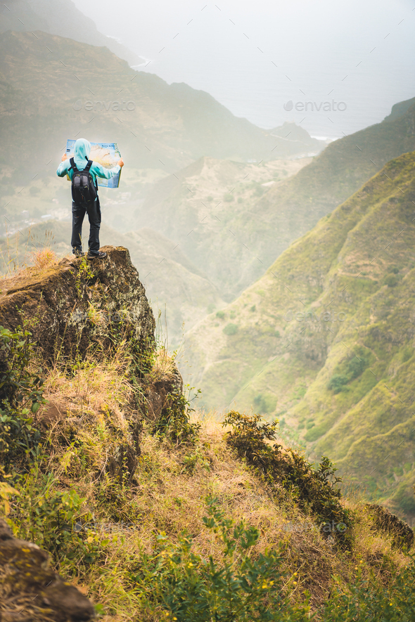 Alone hiker with map of the island staying on a rocky ledge in front of a gorgeous panorama view of - Stock Photo - Images