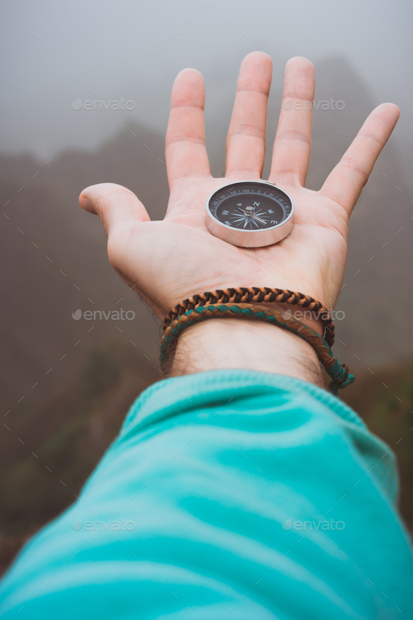 Hand with compass on the rock in front of the monumental mountain range silhouette in the fog - Stock Photo - Images