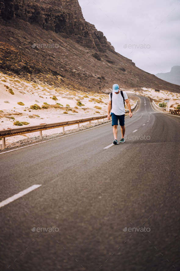 Traveler with backpack standing in the center of an epic winding road. Huge volcanic mountains in - Stock Photo - Images