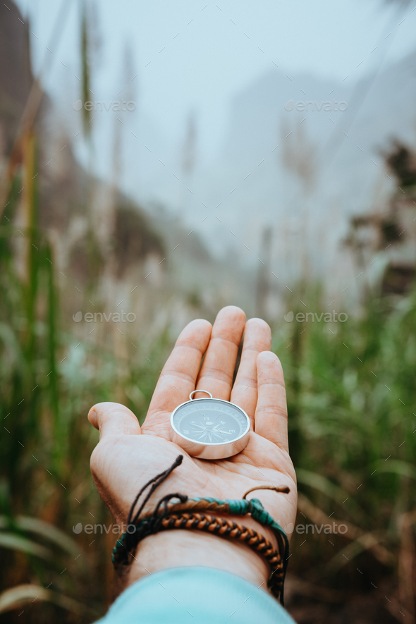 Man arm with compass on the palm stretched out to determine position in mountains on cloudy day - Stock Photo - Images