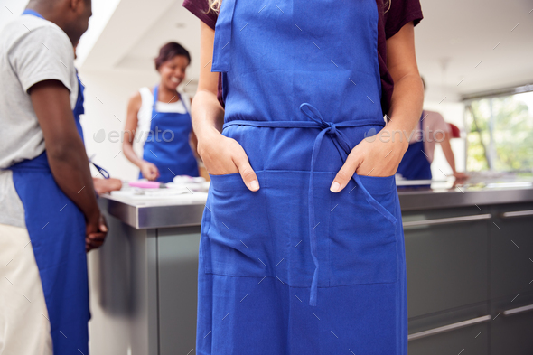 Close Up Of Woman With Hands In Apron Pocket Taking Part In Cookery Class In Kitchen