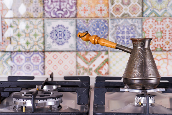 Cooking coffee on a gas stove. Old turkish copper pot for brewing coffee on stove in the kitchen - Stock Photo - Images