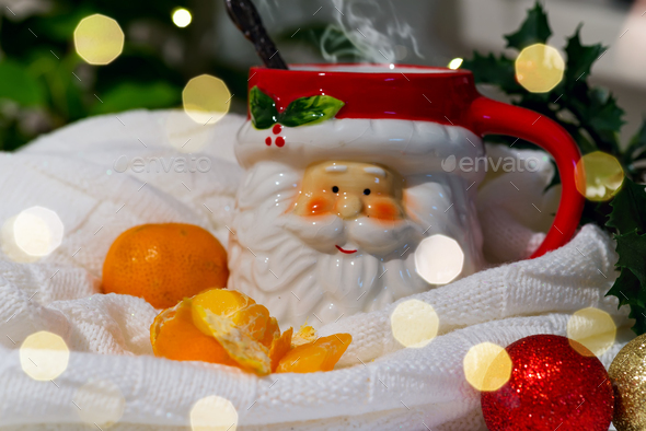 A cup in the form of Santa with hot tea and tangerines in a plaid with highlights on a background of - Stock Photo - Images