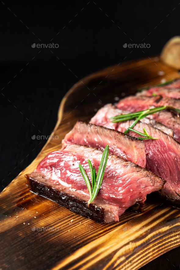 Juicy Beef Rib Eye Steak slices slightly salted, with herbs and spices on wooden board - Stock Photo - Images