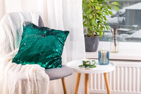 a cup of herbal tea on a table, a knitted wool blanket , green sequin pillow on a chair and candle - Stock Photo - Images