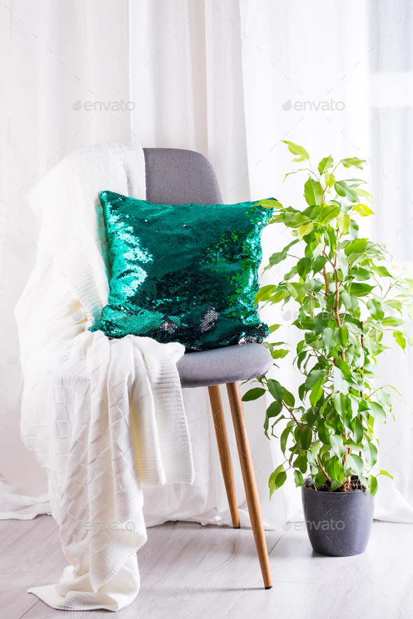 White plaid and green sequins pillow with flower pot on gray armchair over window of living room
