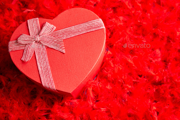 Heart shaped boxed gift, placed on red feathers background - Stock Photo - Images