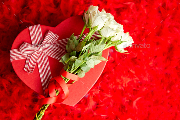 Heart shaped boxed gift, placed on red feathers background - Stock Photo - Images