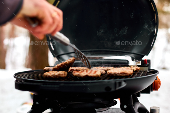 Man grilling steaks on a portable BBQ, Snowy winter barbecue - Stock Photo - Images