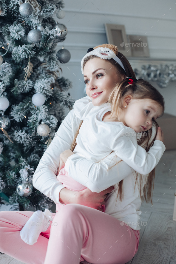 Happy festive mother and daughter hugging sitting together at decorating beautiful Christmas tree - Stock Photo - Images