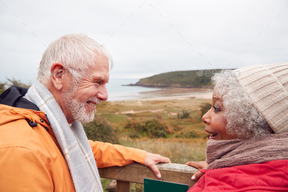 Rear View Of Active Senior Couple Looking Out Over Gate As They Walk Along Coastal Path In Fall