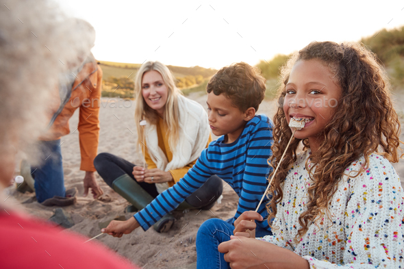 Portrait Of Multi-Generation Family Toasting Marshmallows Around Fire On Winter Beach Vacation
