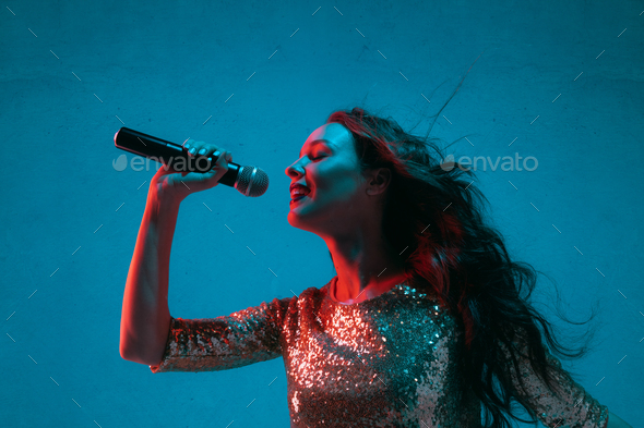 Caucasian female singer portrait isolated on blue studio background in neon light - Stock Photo - Images