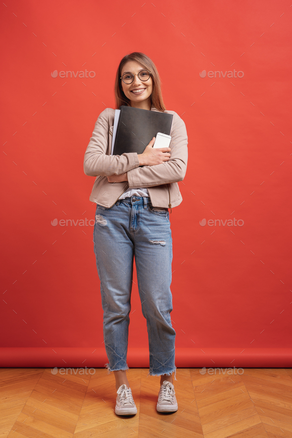 Young smiling student or intern in eyeglasses standing with a folder on red background. - Stock Photo - Images
