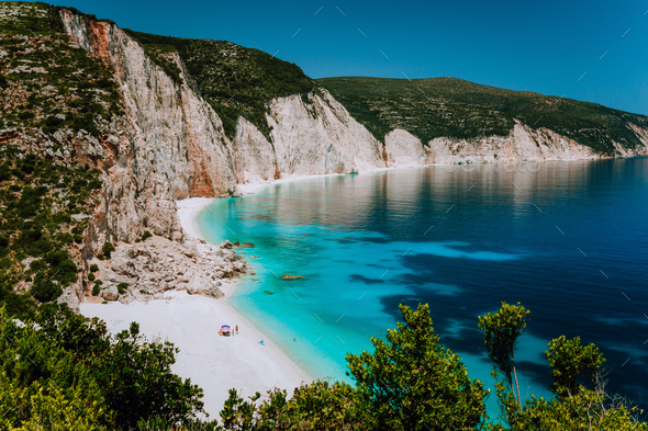 Amazing Fteri beach lagoon, Kefalonia, Greece. Tourists under umbrella chill relax near clear blue - Stock Photo - Images