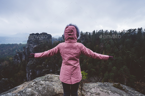 Hiker female in outdoor clothing raised hands on the top of a mountain and enjoying view of cliffs - Stock Photo - Images
