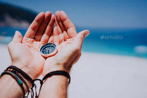 Open hand palms with metal compass on the sandy beach. Searching your way concept. Blue sea in - Stock Photo - Images