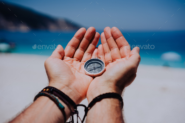 Open hand palms with metal compass on the sandy beach. Searching your way concept. Blue sea in - Stock Photo - Images