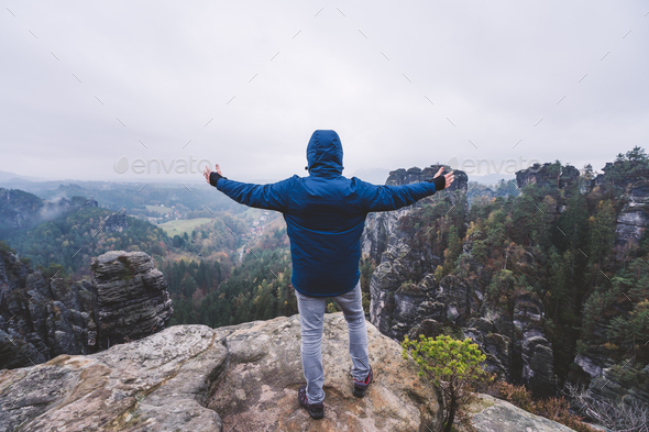 Hiker in outdoor clothing raised hands on the top of a mountain and enjoying view of cliffs ridge - Stock Photo - Images