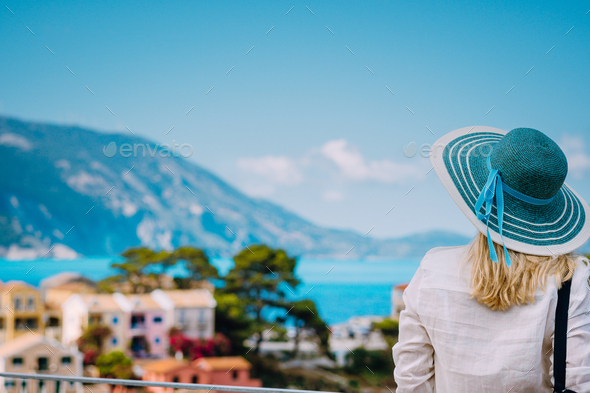 Tourist woman wear blue sunhat and white clothes admire view of colorful tranquil village Assos on - Stock Photo - Images