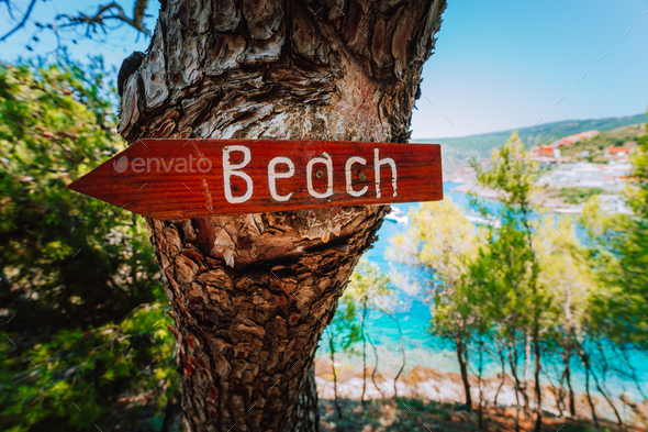 Assos village in morning light, Kefalonia. Greece. Beach wooden arrow sign on a pine tree showing - Stock Photo - Images
