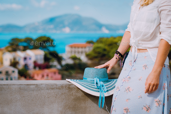 Blue sunhat laying on sidewalk wall. Tourist woman enjoying view of colorful tranquil village Assos - Stock Photo - Images
