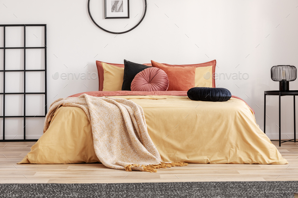 Black round velvet pillow on yellow duvet in trendy bedroom interior with king size bed