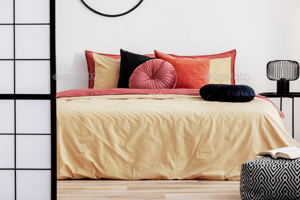 Black round velvet pillow on yellow duvet in trendy bedroom interior with king size bed