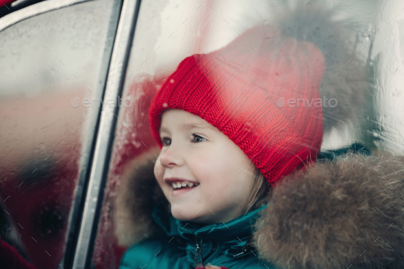 Smiling cute winter girl in red hat sitting in car having fun - Stock Photo - Images