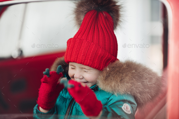 Smiling cute winter girl in red hat sitting in car having fun - Stock Photo - Images