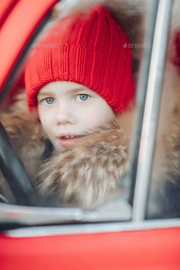 Smiling cute winter boy in red hat sitting in car having fun - Stock Photo - Images