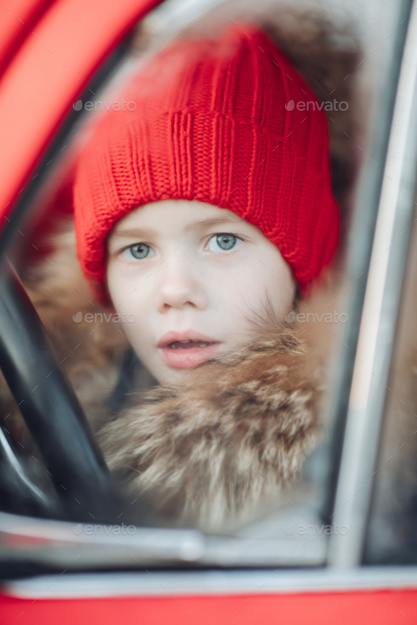 Smiling cute winter boy in red hat sitting in car having fun - Stock Photo - Images