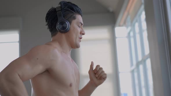 Muscular athletic man listen to music and running on treadmill