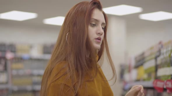 Portrait of Focused Redhead Caucasian Woman with Green Eyes Shopping in Wine Shop. Confident alt