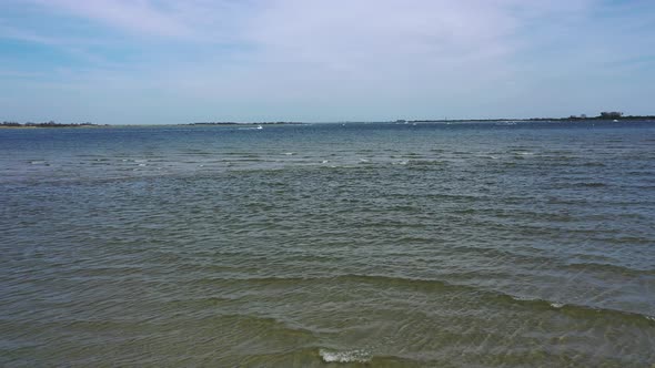 A low angle drone shot over a beach, looking out at the water & the horizon. It is at low tide on a alt