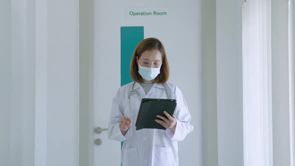 Asian female doctor reading patient history report while walking along hospital corridor