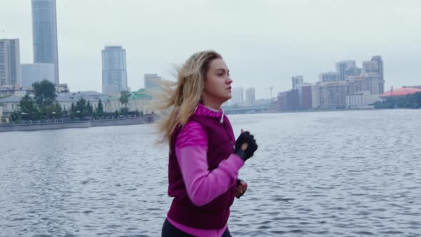 Beautiful Blonde Girl Runs Along Urban Embankment alt