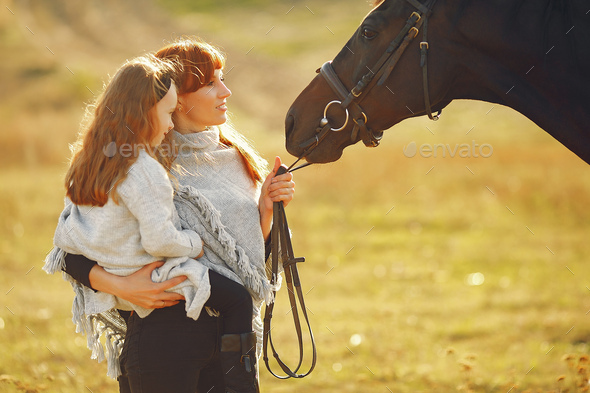 Mother and daughter in a field playing with a horse - Stock Photo - Images