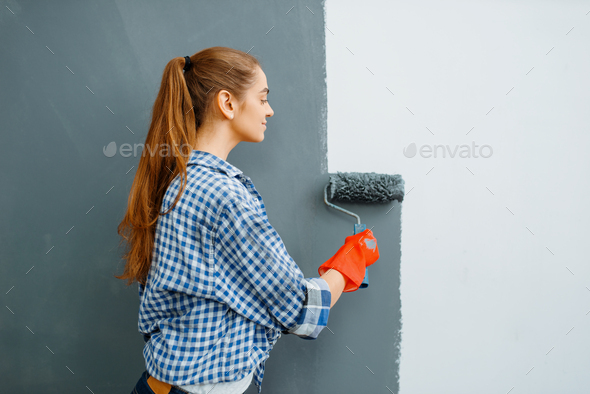 Cheerful female house painter paints walls indoor - Stock Photo - Images